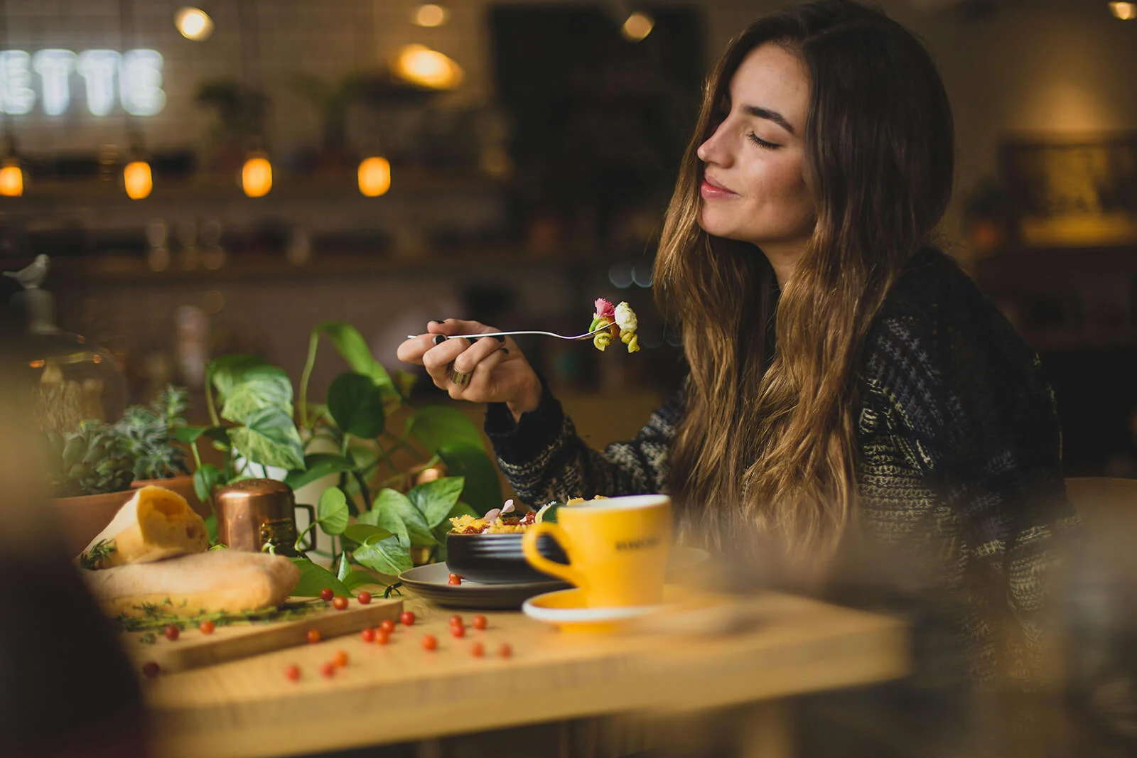 Donna che mangia un'insalata colorata in un ambiente accogliente con piante e luci soffuse